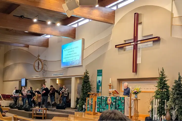 A photo of the pastor standing in front of Trinity Lutheran Church in Eau Claire, WI, with a cross behind him, and a band of musicians playing music to his right.