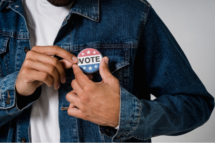 A person pinning a "vote" button on their jacket.